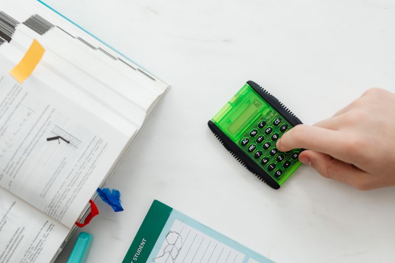 Hand using a calculator next to an open textbook for AP coursework