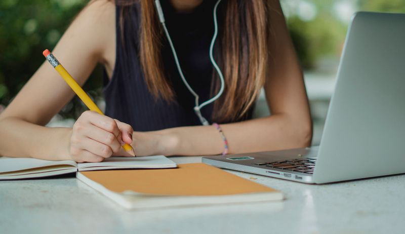 Student writing tracking details for each school on a college application spreadsheet