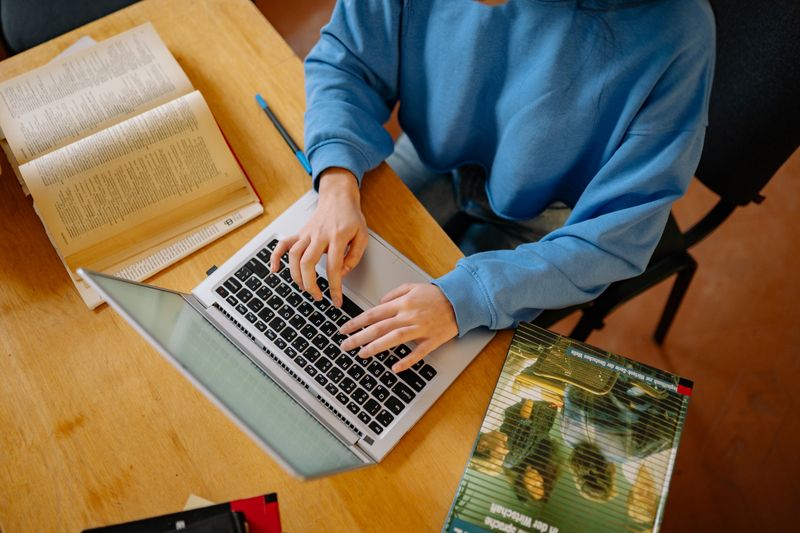 Student typing on a laptop while managing a college application tracker