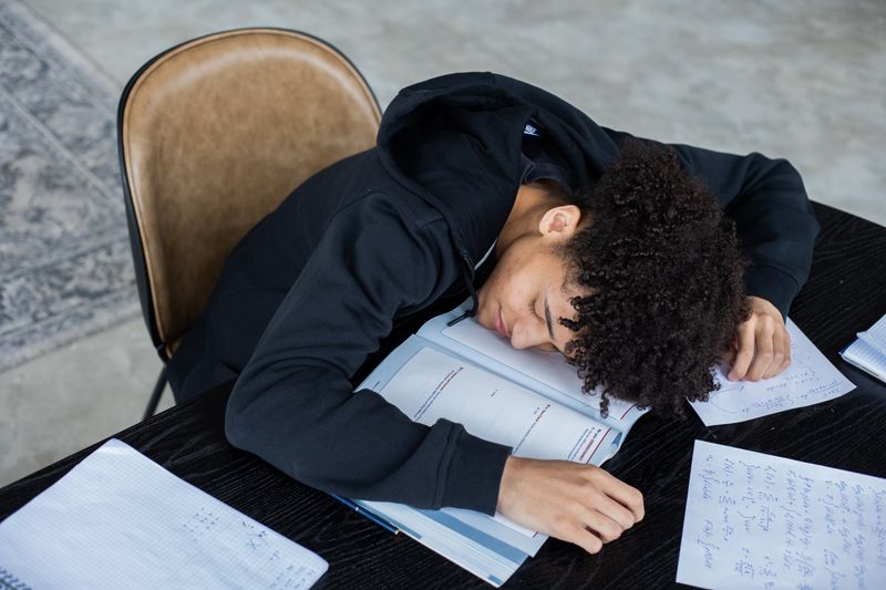 Exhausted student resting head on a desk covered in papers