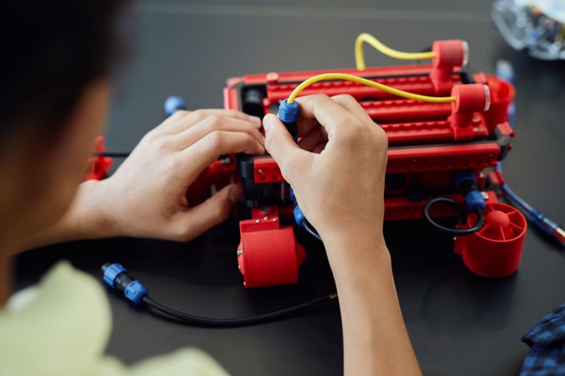 Hands working together on a robotics prototype representing Conrad Challenge team eligibility