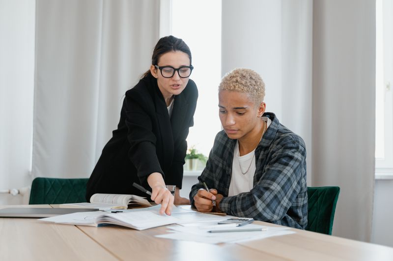 Mentor guiding a high school student through research notes at a desk