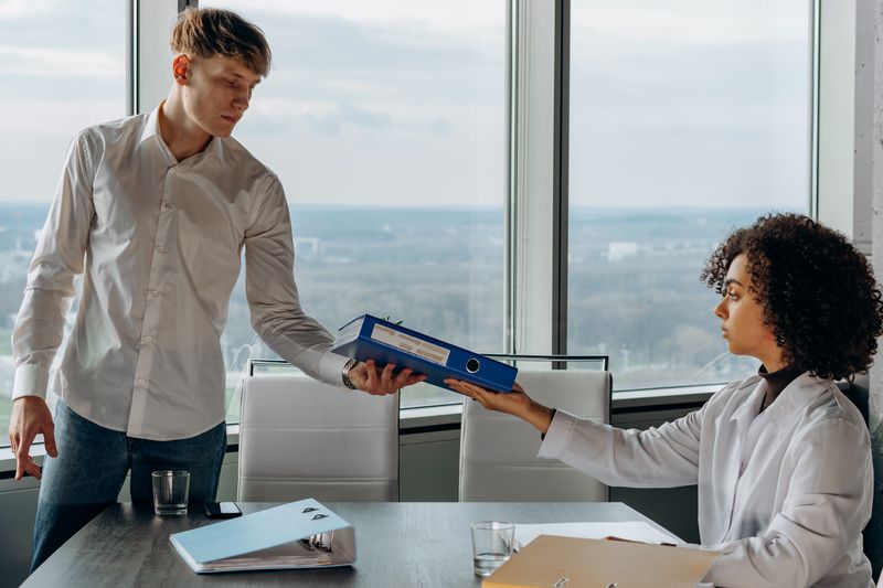 Two colleagues exchanging documents in an office overlooking the city during a high school internship in Dallas