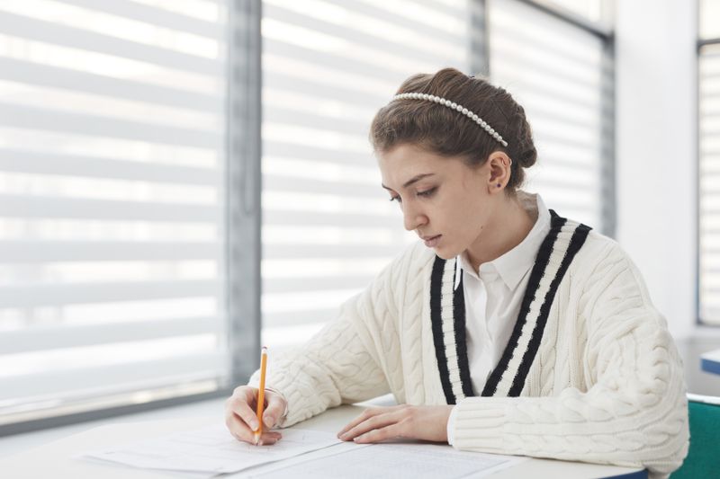 Student writing at a desk near a window working on essay revisions