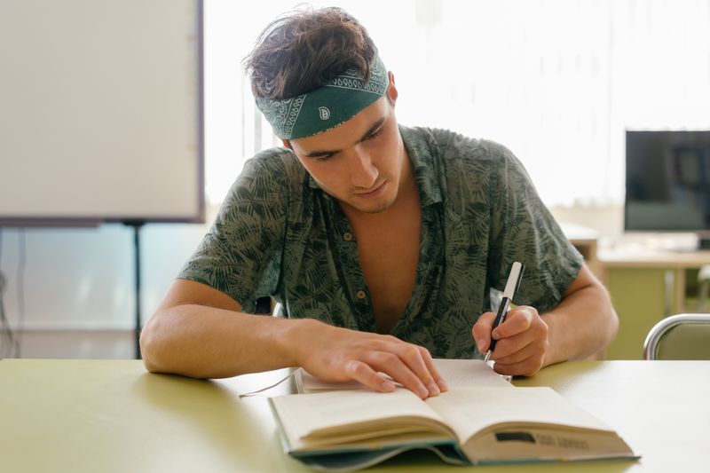 Student writing in a notebook considering how colleges view IB versus AP coursework