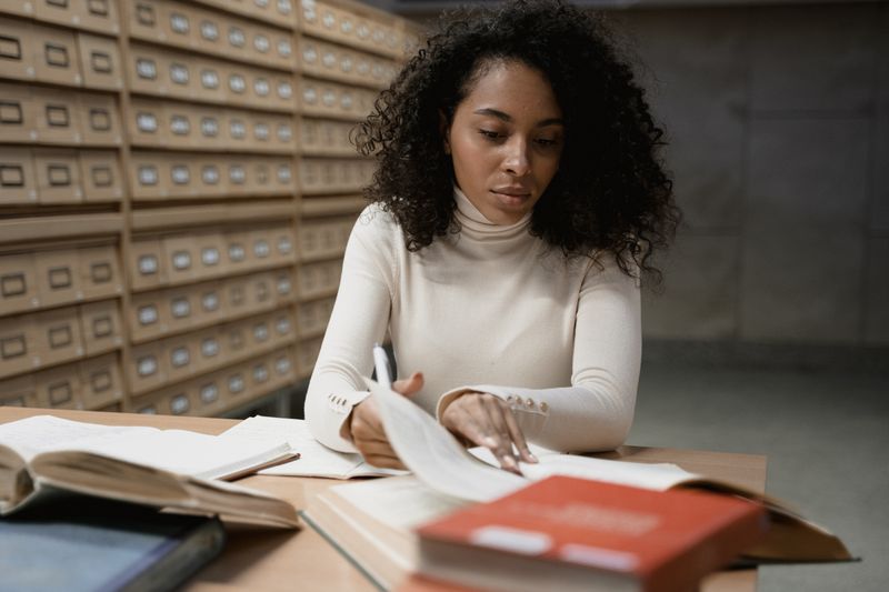 Student writing citations while reviewing books in a library card catalog area