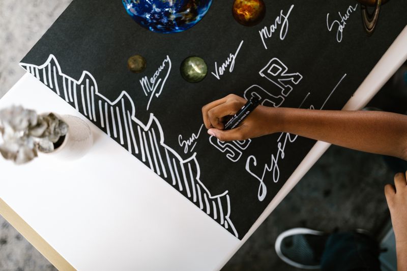 Hands writing planet names representing the NASA SEES earth and space science program