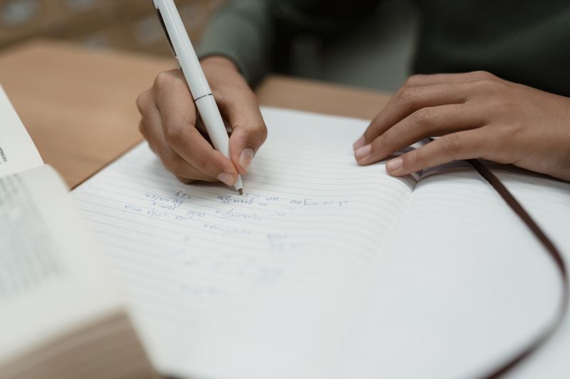 Hands writing research notes next to an open reference book