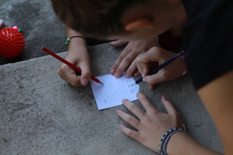 Hands solving a cipher puzzle for a Science Olympiad Codebusters event
