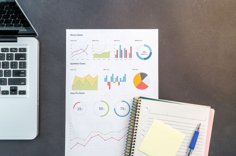 Data charts and notebook arranged on a desk next to a laptop