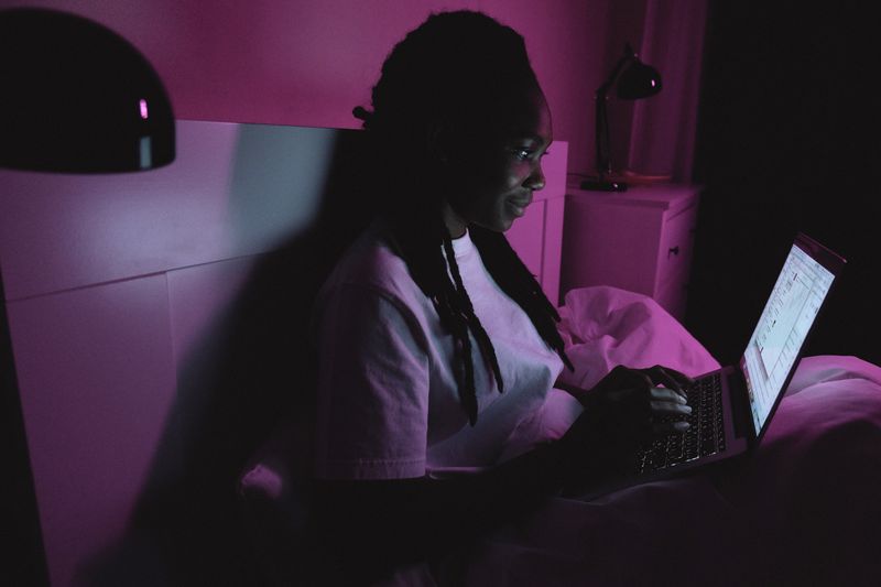 Student submitting a college application on a laptop late at night in bed