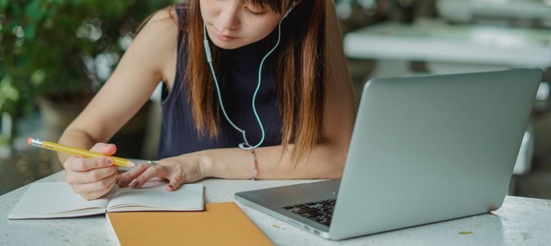 Student writing an application essay by hand next to an open laptop