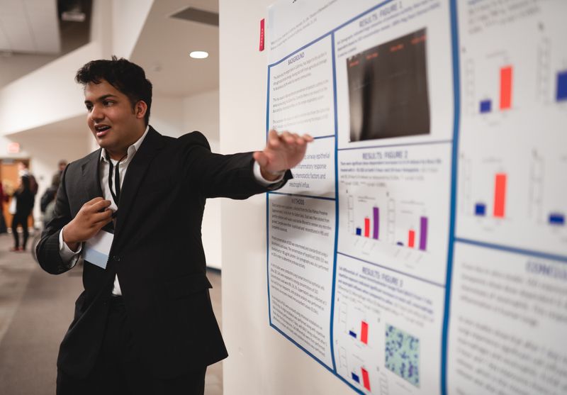 Student presenting research findings on a poster board at a symposium