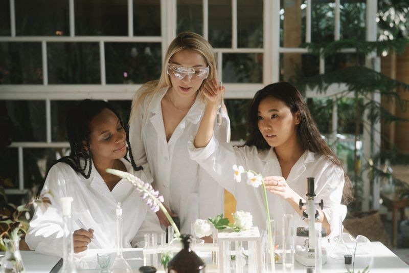 Three diverse students in white lab coats working together in a research setting